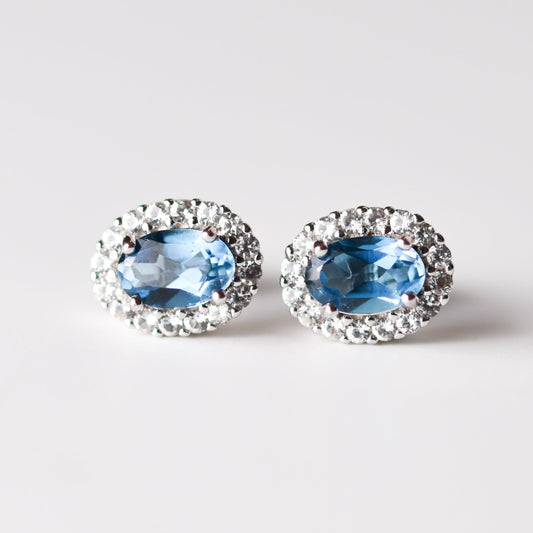 Aretes tipo stud con topacio London Blue y halo de zafiros blancos de laboratorio