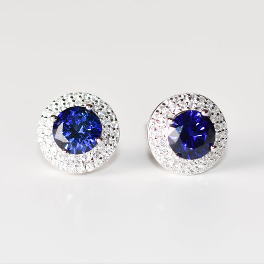 Aretes tipo stud con zafiro azul redondo (1.5 ct) y halo de zafiros blancos