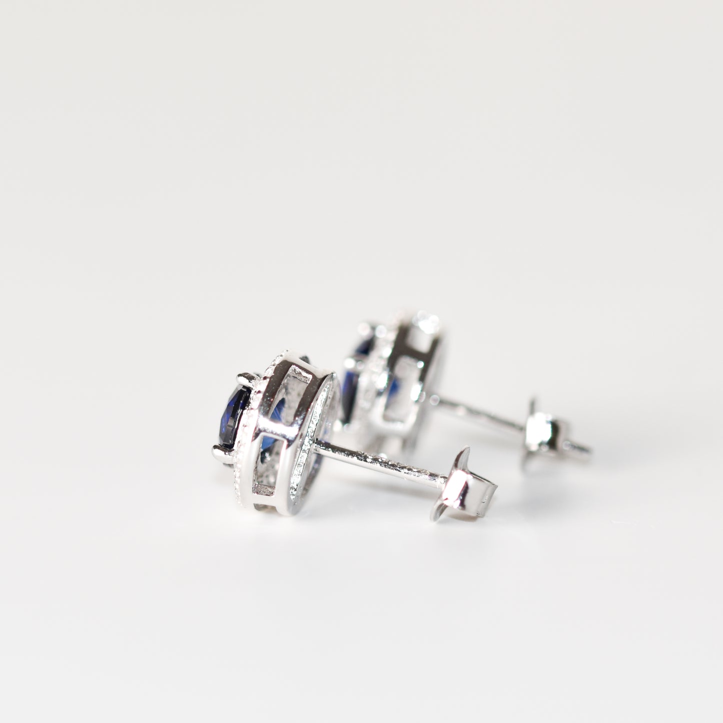 Aretes tipo stud con zafiro azul redondo (1.5 ct) y halo de zafiros blancos
