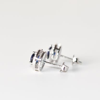 Aretes tipo stud con zafiro azul redondo (1.5 ct) y halo de zafiros blancos