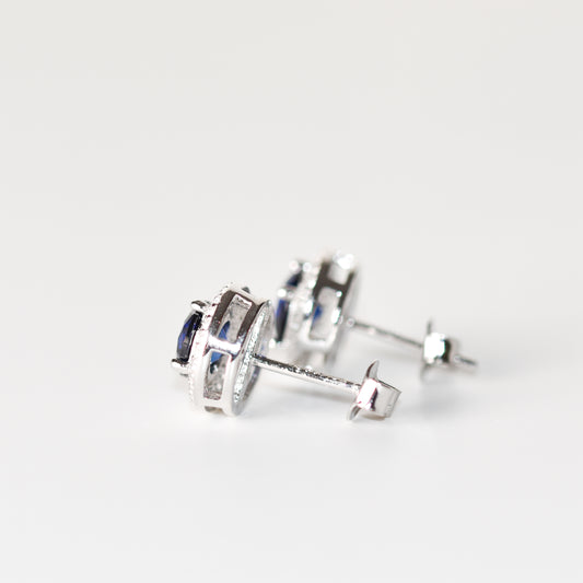 Aretes tipo stud con zafiro azul redondo (1.5 ct) y halo de zafiros blancos