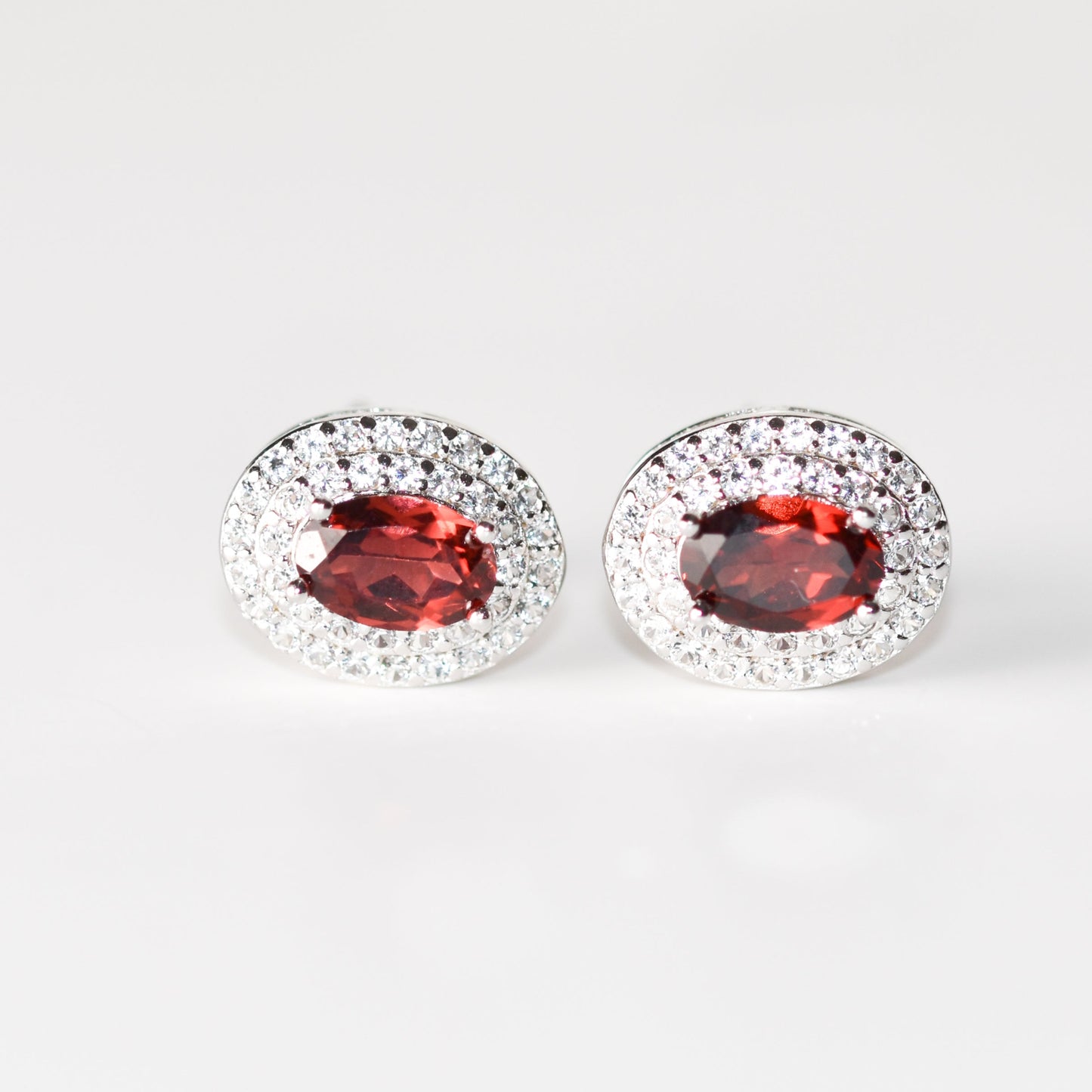 Aretes tipo stud con granate natural y halo de zafiros blancos de laboratorio